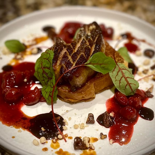 Seared foie gras on brioche toast with cherry compote, balsamic glaze, and microgreens on a white plate.