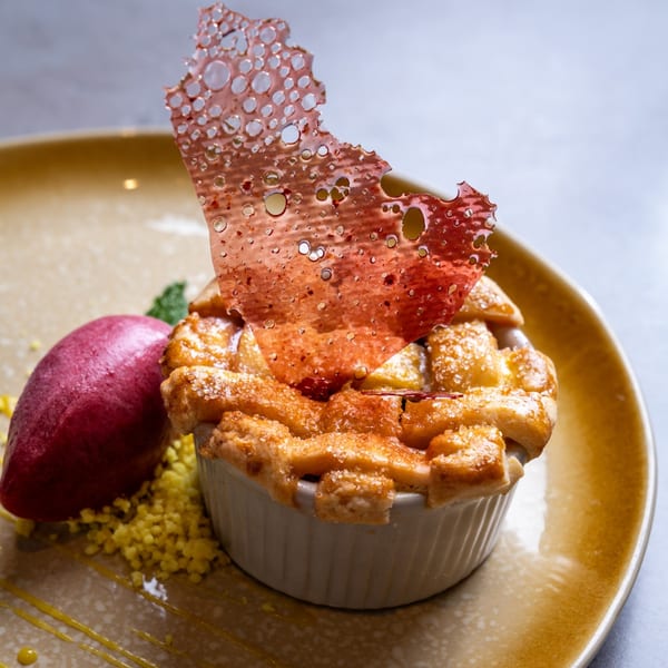 A lattice-top fruit crumble with a decorative sugar shard and a scoop of berry sorbet.