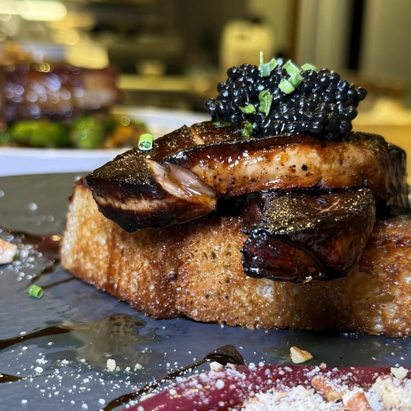 Seared foie gras and caviar on toasted brioche, garnished with chives and a balsamic glaze.