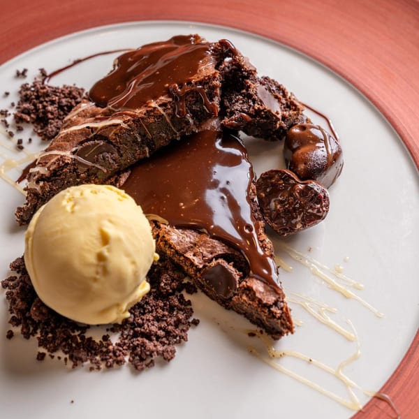 Chocolate brownie slices with chocolate sauce, cookie crumbles, and a scoop of vanilla ice cream.